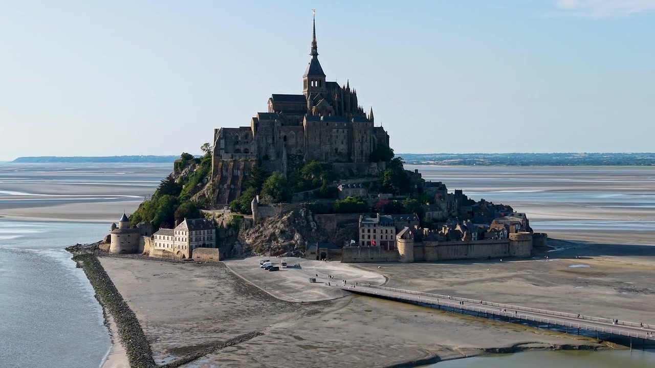 Vista orbital de drone de Mont Saint-Michel, com um movimento panorâmico suave para a esquerda, exibindo a icônica abadia medieval, ilha fortificada e vila histórica.