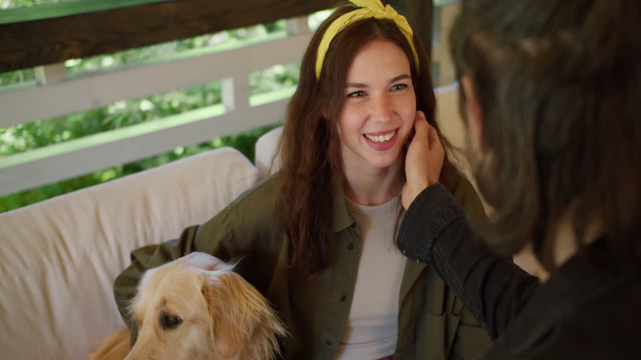 The brunette guy strokes the brunette girl on the cheek. A girl with a yellow bandage in a green sweater, a dog sits near the girl