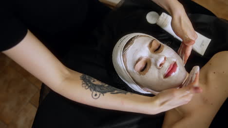 beautician's hands slowly massaging female face applying white mask. spa procedures for beauty and health. close up.