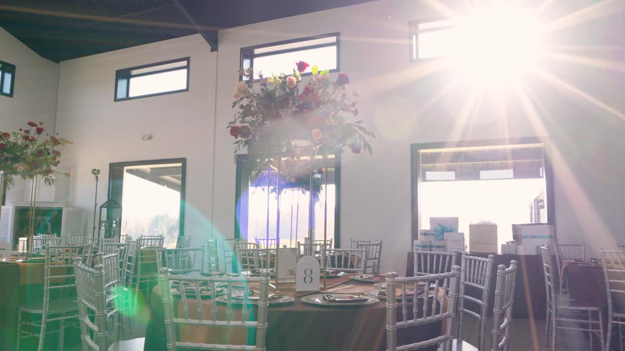Slow push-in on a reception table adorned with floral centerpieces, enhanced by beautiful sunflare. Elegant wedding or event setup with a dreamy, natural light touch.