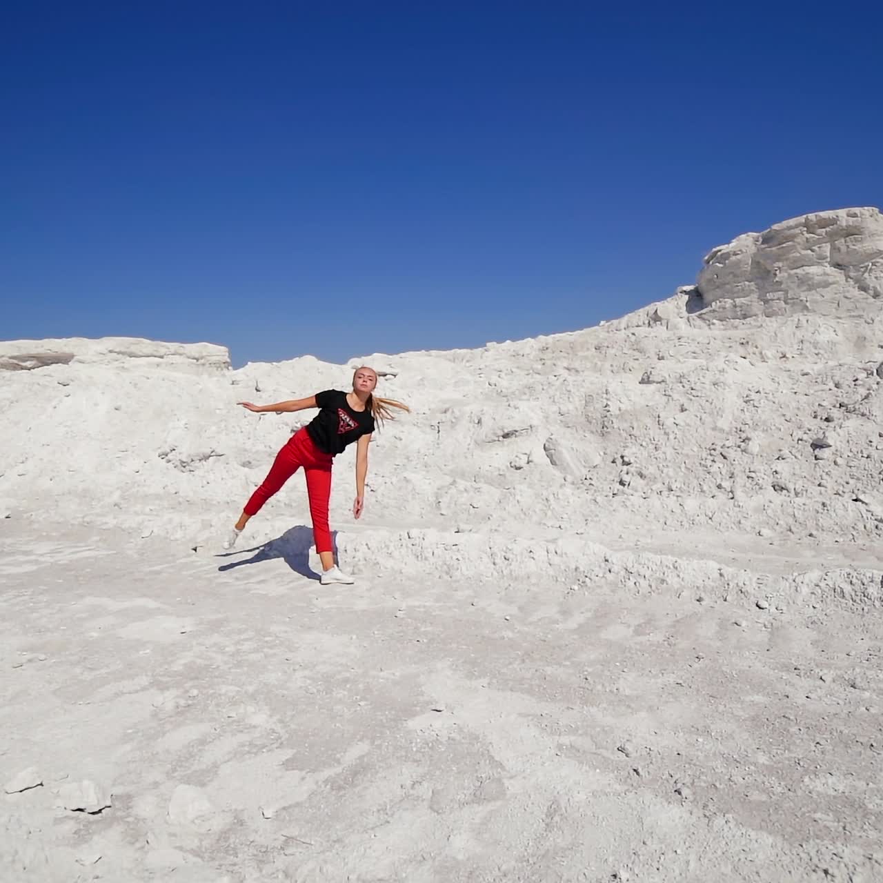Girl making jump with a turn on the white rocky ground. Female dancer showing the dance move outdoors. Blue sky backdrop