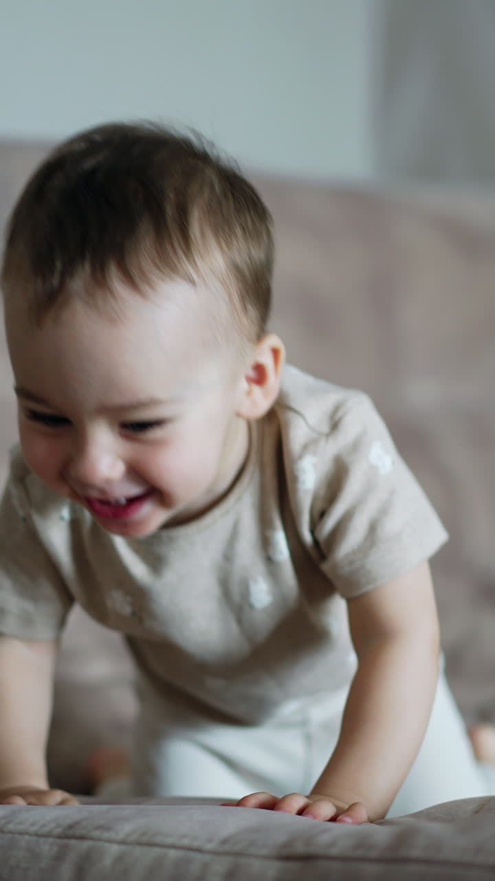Adorable smiling kid jumps on the big soft sofa. Baby pushes the pillow happily. Vertical video