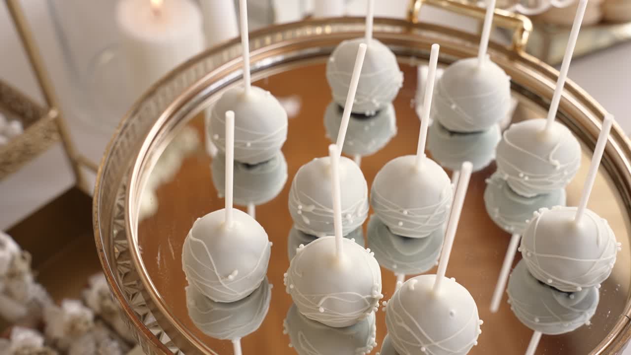 A group of dessert pops sits on a shiny silver tray. They are white and round, with stick handles. The tray has a reflective surface showing the treats clearly