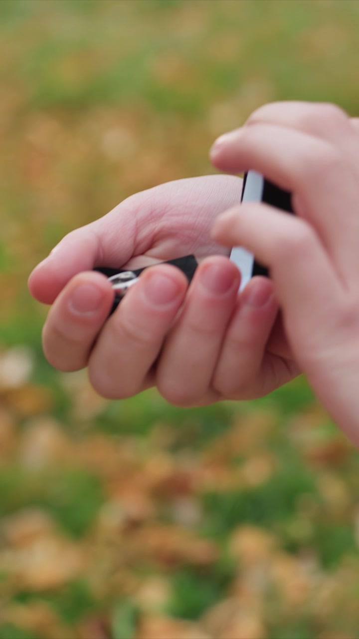 Outdoor close up focusing on paired human appendages. Close up view shows two pairs touching same tiny thing. Outdoor grassy setting with scattered fallen leaves on ground