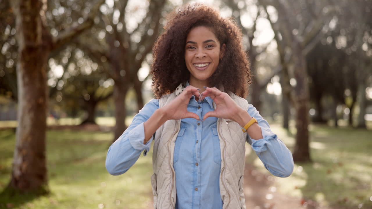 Woman making heart shape with hands in park
