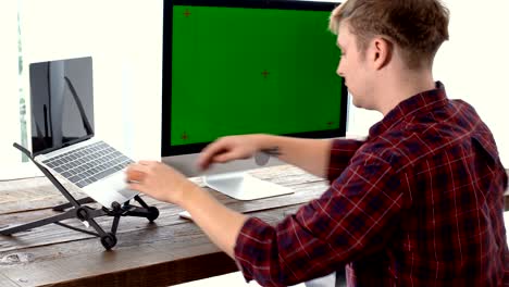 young freelancer man working with laptop and looking green screen monitor