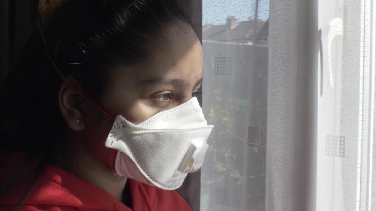 명상적으로 커튼을 통해 실내에서 ffp 3 마스크를 착용한 여자 아이