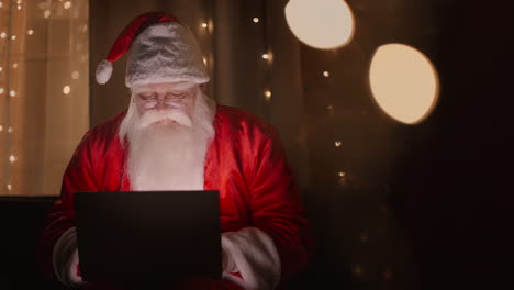 santa claus works with a laptop at night in the light of christmas lights