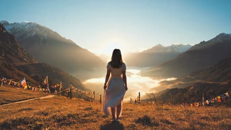 young woman in a white dress is enjoying a breathtaking sunrise over a misty valley surrounded by majestic mountains, with colorful prayer flags adding a spiritual touch to the serene landscape