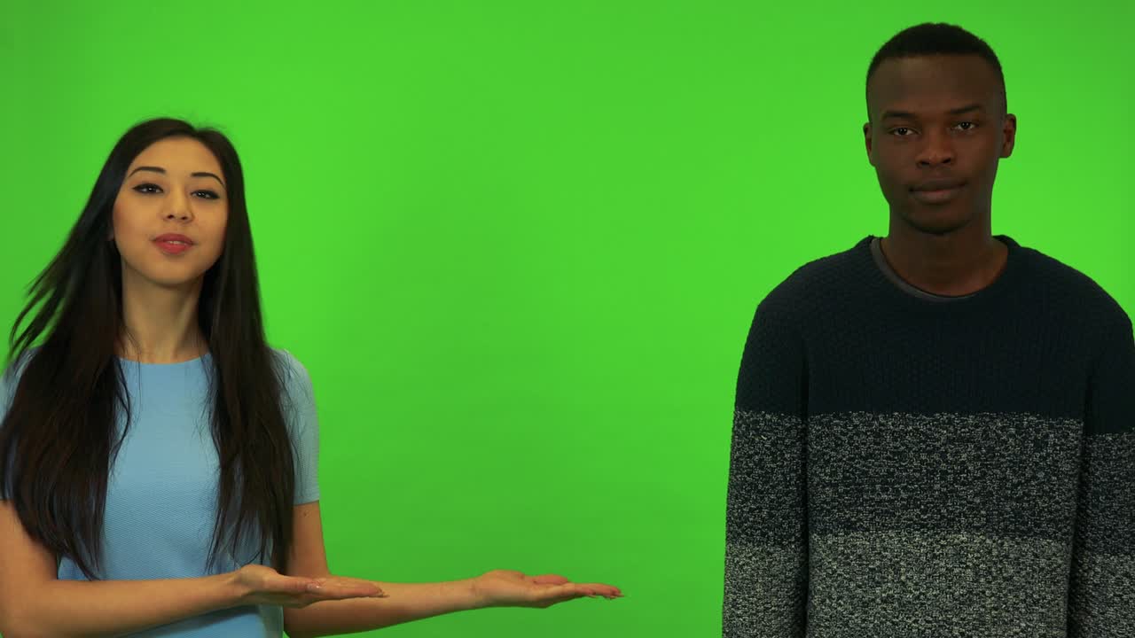 una joven asiática y un joven negro presentan algo - estudio de pantalla verde