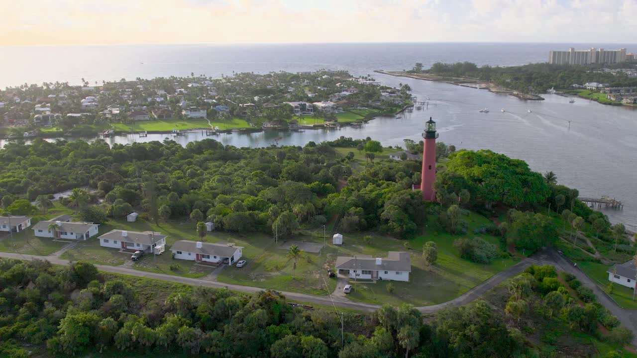 Aerial view of scenic coastal bluff featuring a tall red lighthouse, leafy canopy, and surrounding bay dotted with residential neighborhoods in Jupiter, Florida