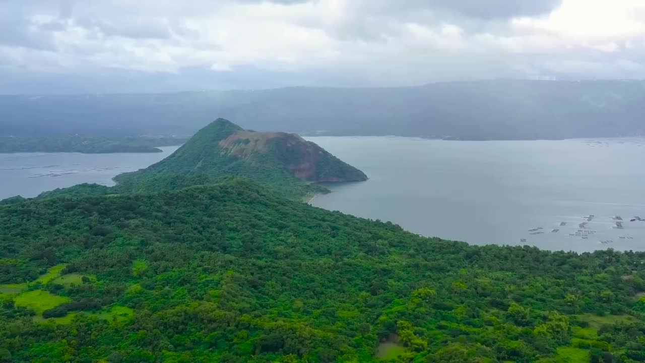 Aerial drone footage flying over Taal lake or Bombon lake in Philippines during a cloudy day. Large mountain is in the lake that is surrounded by green landscape and jungle. Cinematic drone footage.