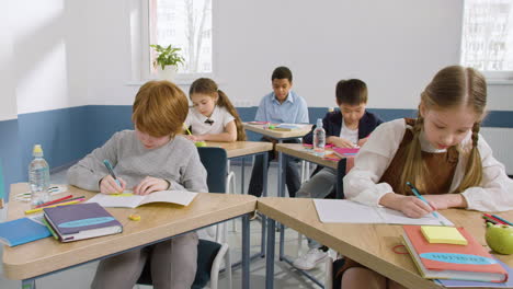 grupo multiétnico de estudiantes sentados en pupitres en clase de inglés levantando los brazos para responder a la pregunta del profesor