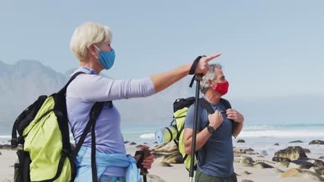 senior hiker couple wearing face masks with backpacks and hiking poles pointing towards a direction