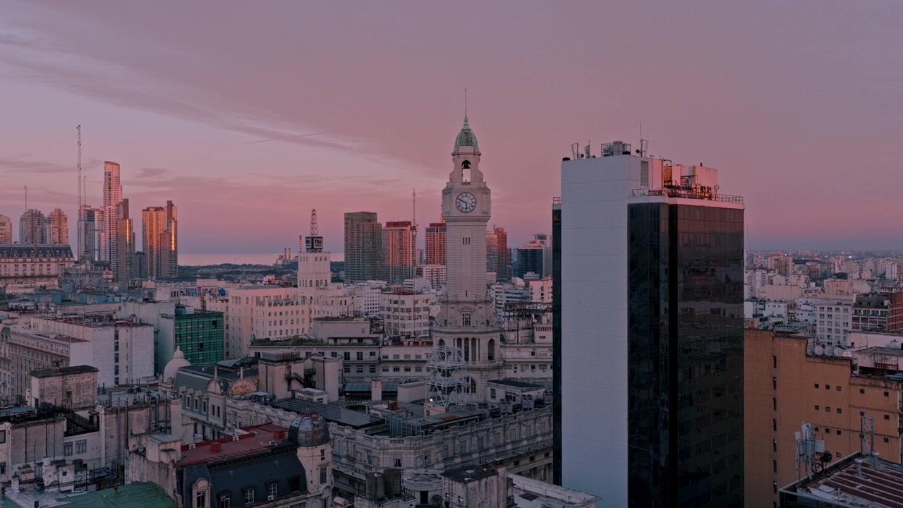 Tomada cinematográfica de drone panorâmica para a esquerda sobre o centro de Buenos Aires revelando a torre do relógio da Legislatura, arquitetura histórica e horizonte moderno sob a luz quente do pôr do sol