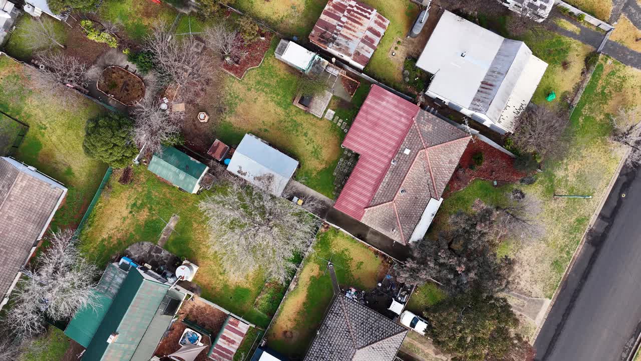 Drone camera smoothly glides above suburban homes, gardens, and driveways in Coonabarabran, New South Wales, under natural daylight with steady overhead movement