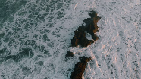 drone footage taken of wild crashing waves on beach and rock early sunset asia