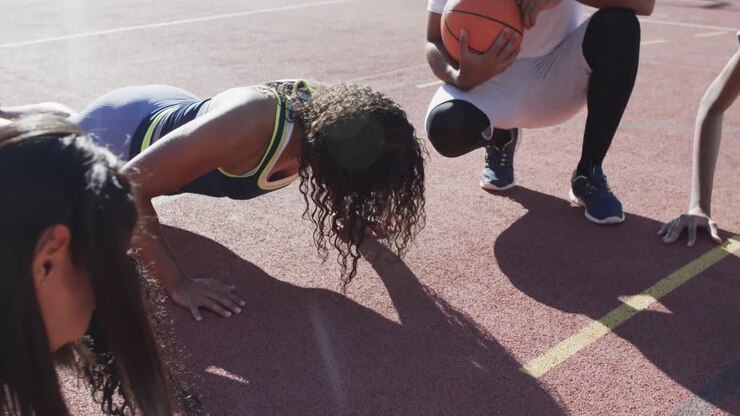 Glückliches, vielfältiges weibliches Basketballteam beim Training mit männlichem Trainer auf sonnigem Spielfeld, in Zeitlupe.