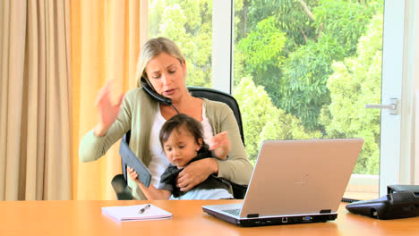 young mother trying to do office work with unruly baby on lap