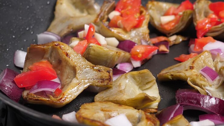 Cooking artichoks and vegetables on frying pan. Closeup