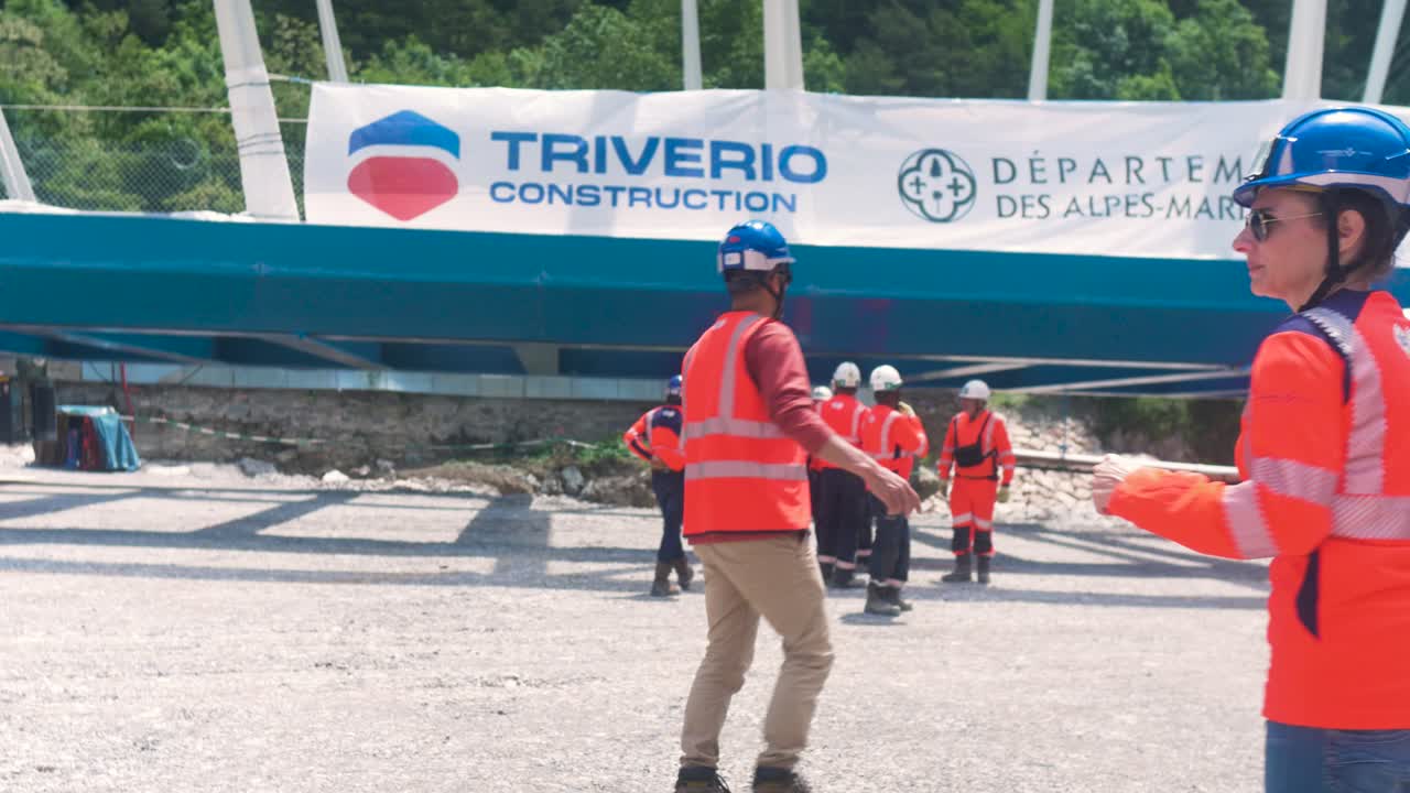 Construction workers coordinate bridge rigging at a site in Tende, South of France under bright sunlight