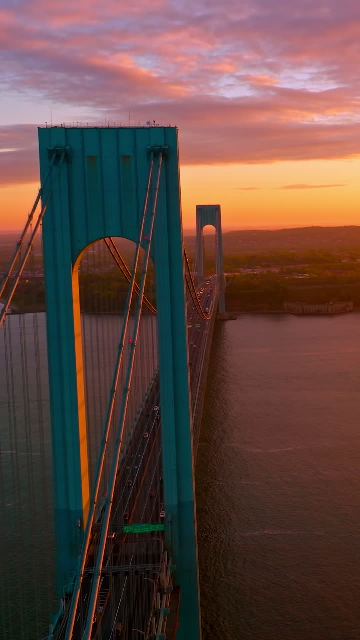 Whitestone bridge with cars moving along it. Pink and orange colors at sundown in New York. Aerial view. Vertical video