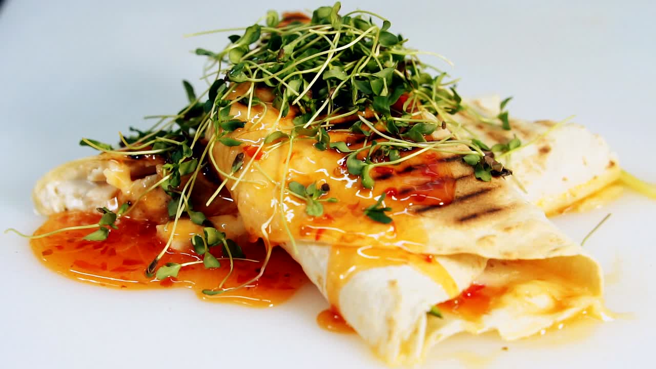 Beautiful presentation of cooked pita in the restaurant. Delicious appetizer decorated with red sauce and green sprouts. Tasty snack rotating. Close-up