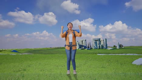 full body of asian female hiker with mountaineering backpack screaming goal celebrating the success while traveling in stonehenge