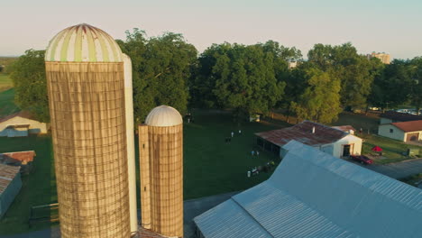 aerial orbiting closely to large grain silos on farm with barn and trees, 4k