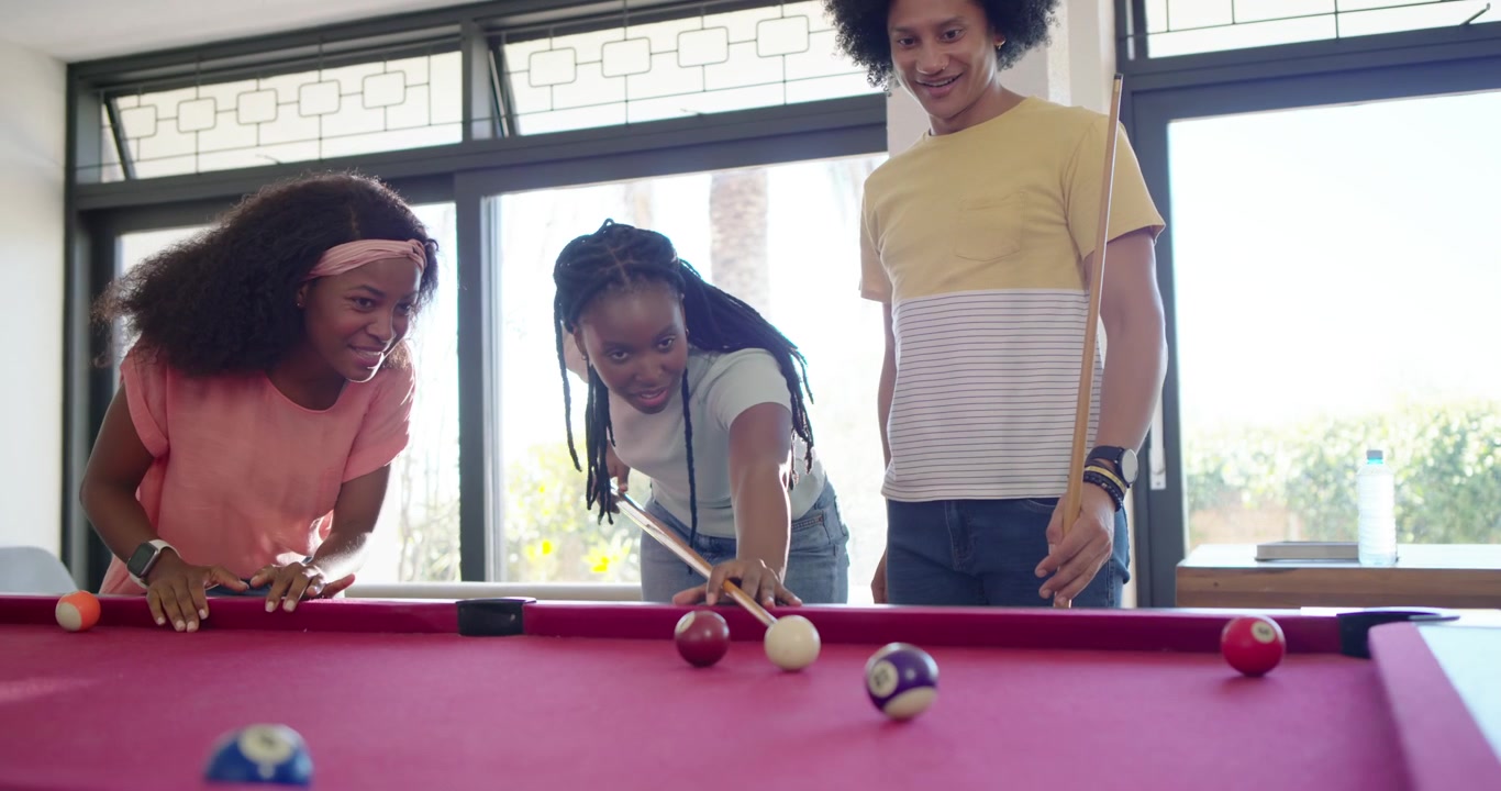 Diverse friends teasing encouraging center woman bridging striking cue ball for fun at pool table