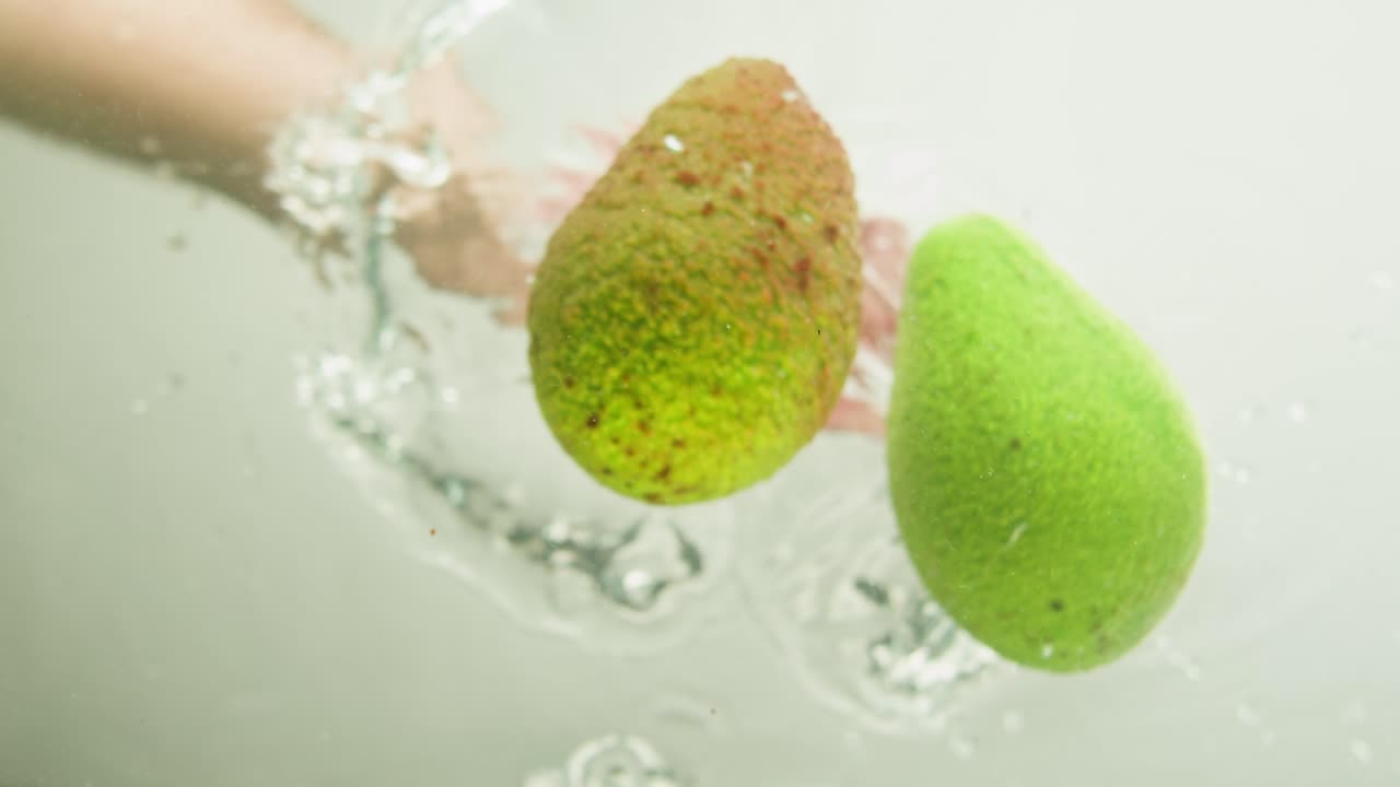 Hands washing avocados under water