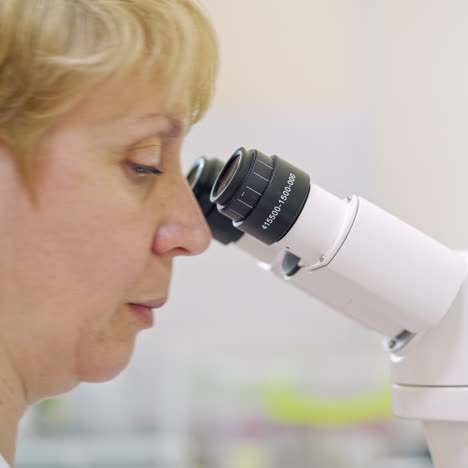 Female scientist looking microscope eyepiece. Portrait of woman scientist looking through microscope. Lab scientist using microscope. Close-up.