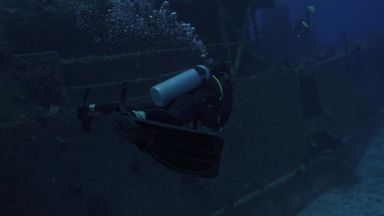 A woman in full scuba gear glides past the massive hull of the ARM General Felipe Xicoténcatl (C-53), Cozumel's premier artificial reef dive site