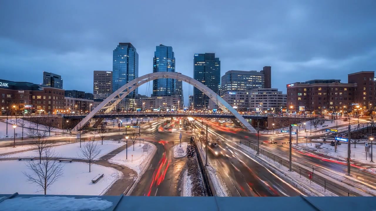 Paisaje urbano nocturno con carreteras nevadas y edificios iluminados bajo un dramático puente de arco – Una cautivadora escena urbana en invierno.