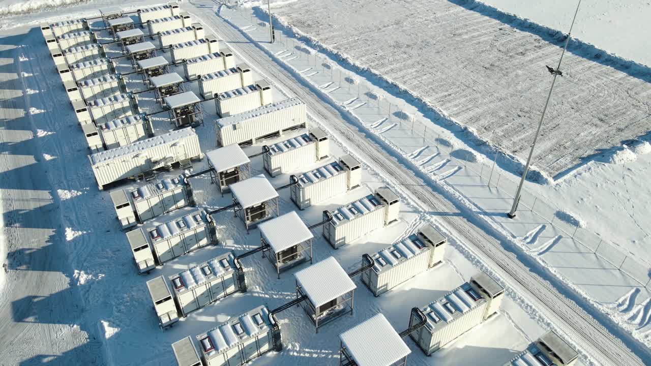 Orbita aerea che rivela un enorme parco di accumulo di energia a batterie da 100 MW e una sottostazione in campi innevati, condizioni invernali che supportano la stabilità della rete elettrica e l'integrazione delle energie rinnovabili. Layout simmetrico dei container