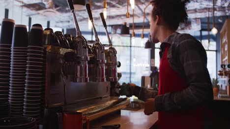 barista masculino de raza mixta con un delantal limpiando la máquina de café y el mostrador