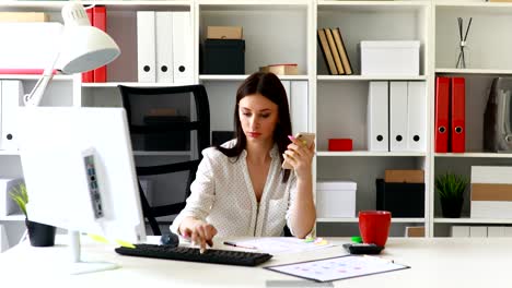 businesswoman working at computer and using smartphone in light office