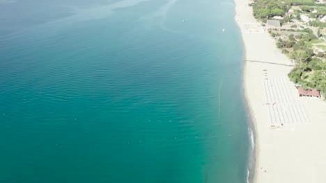 Vista-Aérea-Del-Hermoso-Mar-Mediterráneo-Y-La-Playa-En-Un-Día-Soleado,-Paisaje-Marino-Y-Montaña-En-El-Fondo,-Simeri-Mare,-Calabria,-Sur-De-Italia