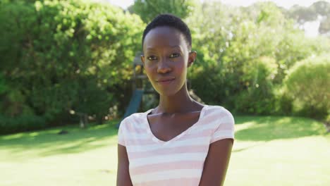 Retrato-De-Una-Mujer-Afroamericana-Parada-En-Un-Jardín-Soleado-Sonriendo-A-La-Cámara