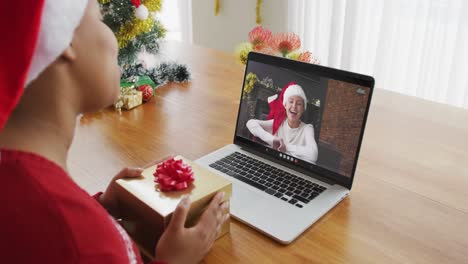 Mujer-Afroamericana-Con-Gorro-De-Papá-Noel-Usando-Una-Computadora-Portátil-Para-Una-Videollamada-Navideña,-Con-Una-Mujer-En-La-Pantalla