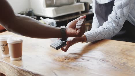 Sección-Media-De-Un-Hombre-Afroamericano-Haciendo-Pagos-Con-Un-Reloj-Inteligente-En-Una-Cafetería,-Cámara-Lenta