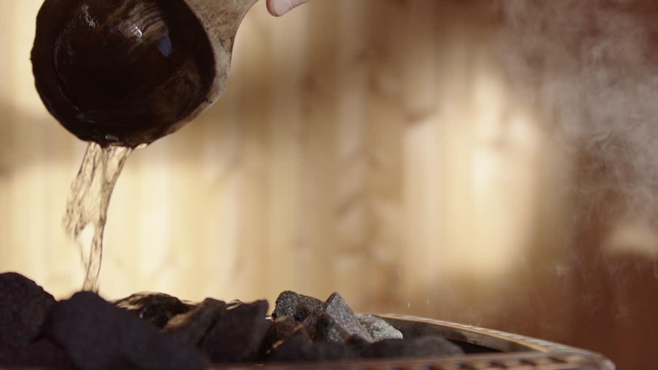 Water poured on heated rocks of stove in wooden sauna, wellness ritual