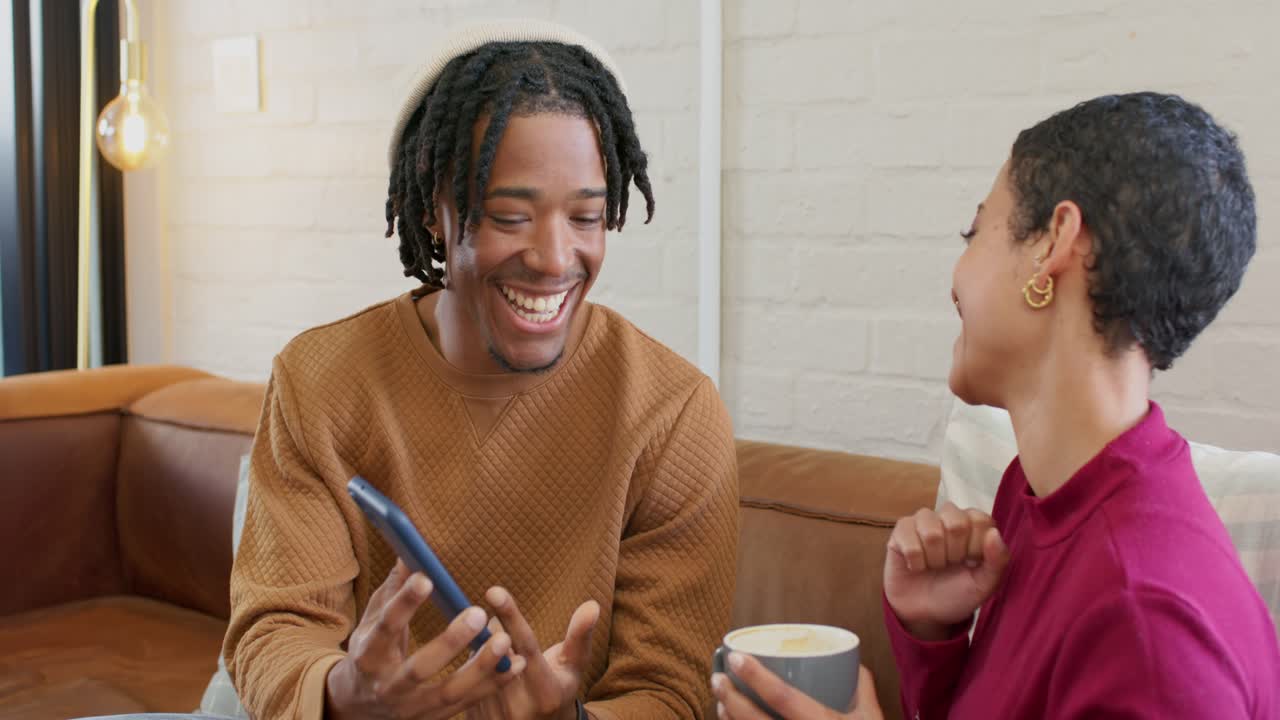 Spotting funny message on smartphone, diverse couple pointing at screen and laughing on couch