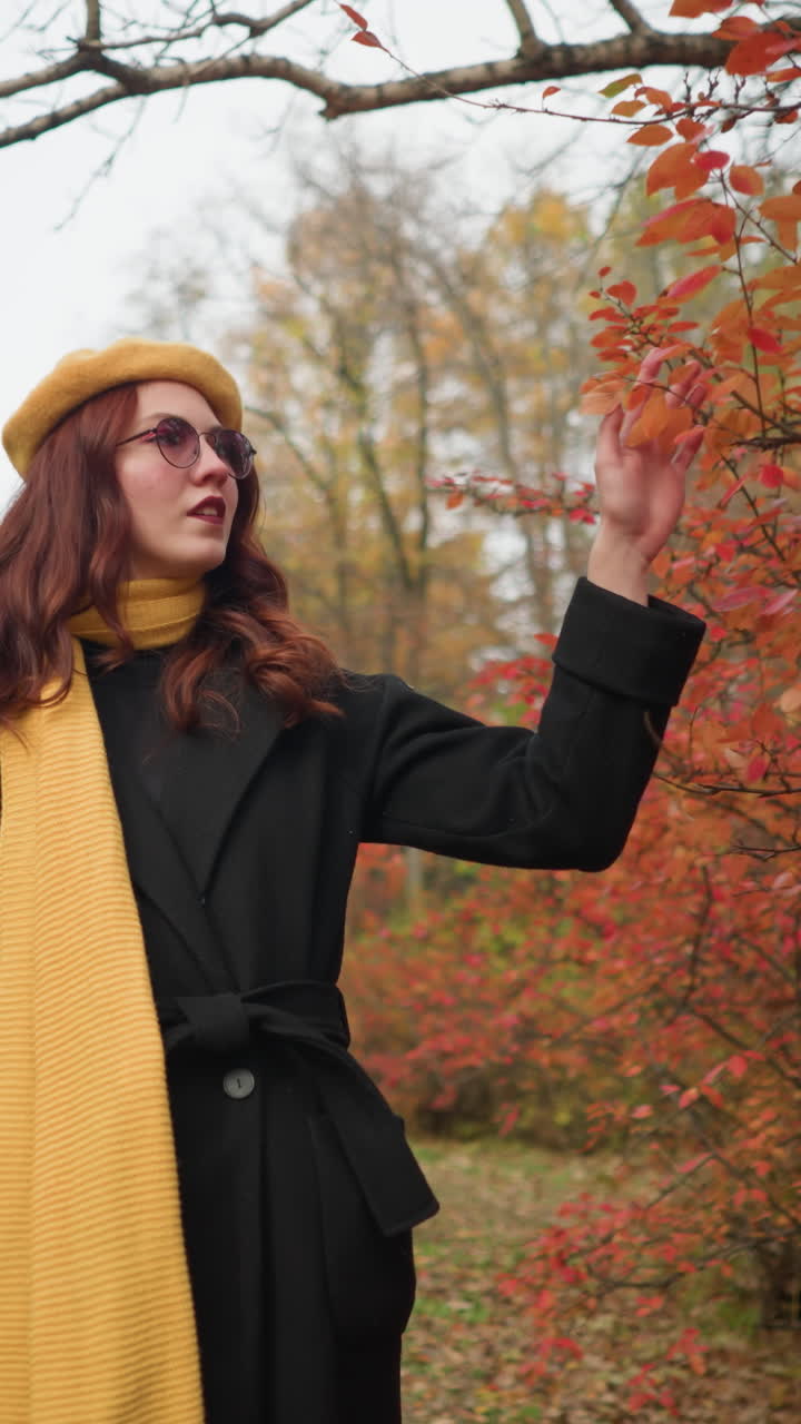 elegante dama con boina amarilla y silenciador explora el camino del otoño, tocando delicadamente hojas rojas vibrantes, encarnando la esencia de la belleza serena del otoño