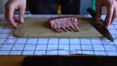 chef sosteniendo una tabla de cortar con un costillar de cordero y un cuchillo de chef encima