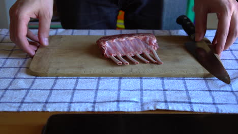 chef holding a cutting board with a rack of lamb and a chef knife on top