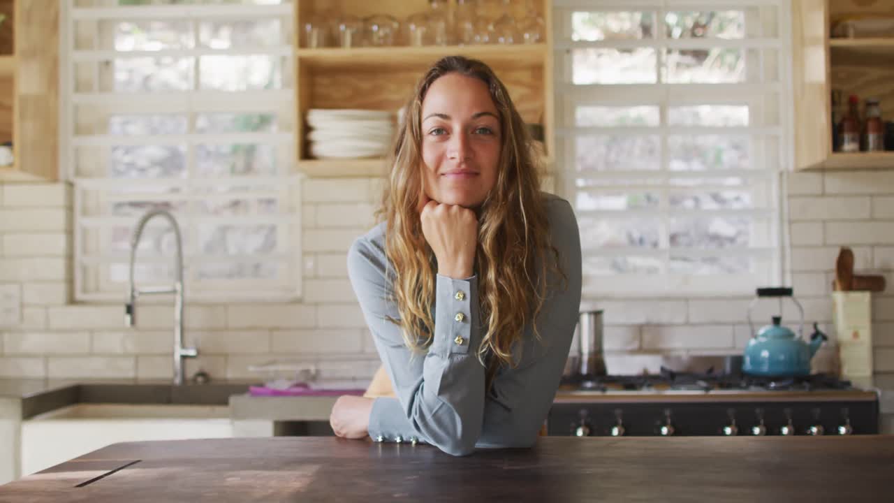 retrato de una feliz mujer caucásica de pie en una cocina de cabaña soleada y apoyada en el mostrador