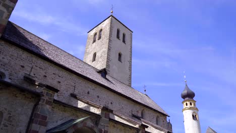 wide tracking shot revealing the exterior and bell tower of the romanesque collegiate church of san candido, italy