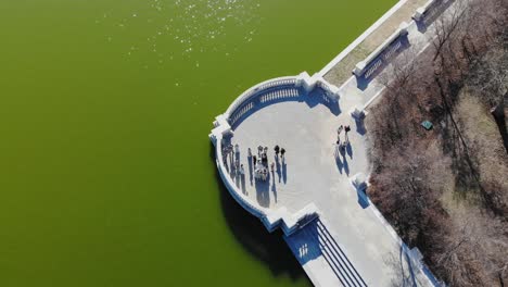 Ascending-aerial-shot-of-a-wedding-party-gathered-by-a-lake-on-Art-Hill-in-Saint-Louis,-Missouri