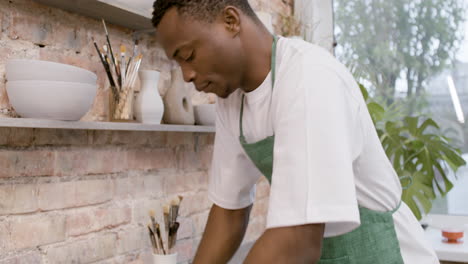 close up view of american clerk in agreen apron kneading clay on top of a table in a pottery workshop